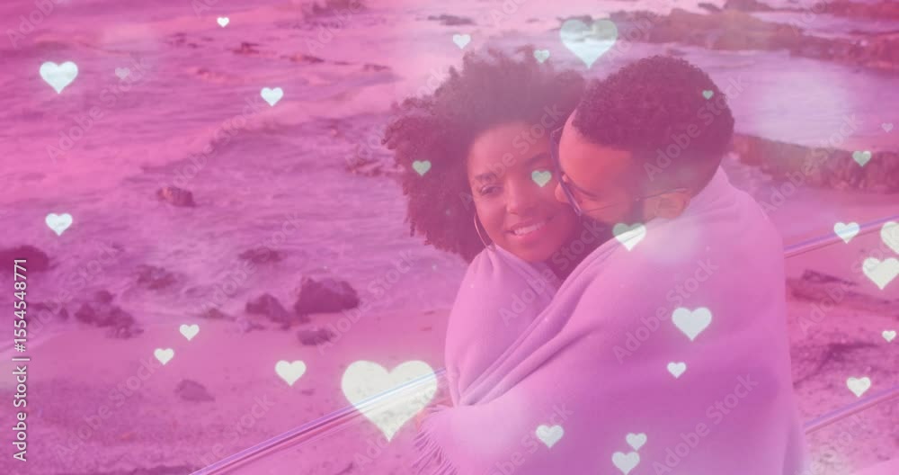 Man wrapping blanket around couple on coastal walkway creating marketing ad with floating hearts