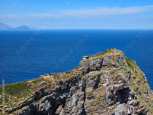 Rocky cliff overlooking the ocean. The ocean is blue and the sky is clear. There are no clouds in the sky in Cape of good hope in South Africa