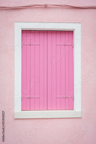 Bright pink wooden shutters on pink wall with white trim on building facade