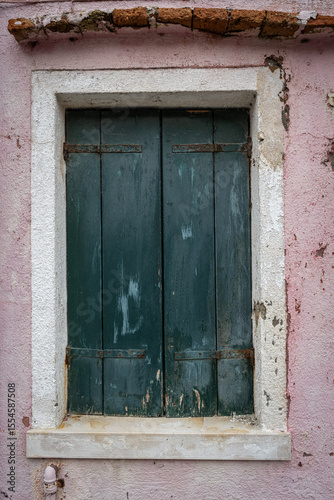 Old weathered green wooden window shutters on pink stucco wall