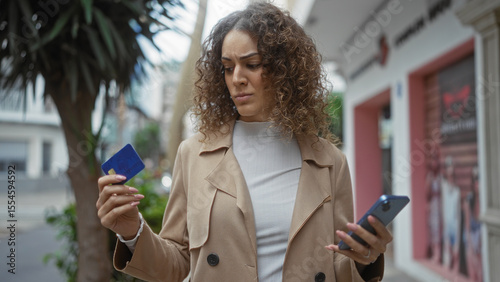 Woman outdoors holding credit card puzzled expression city background stylish coat showing financial concern urban setting