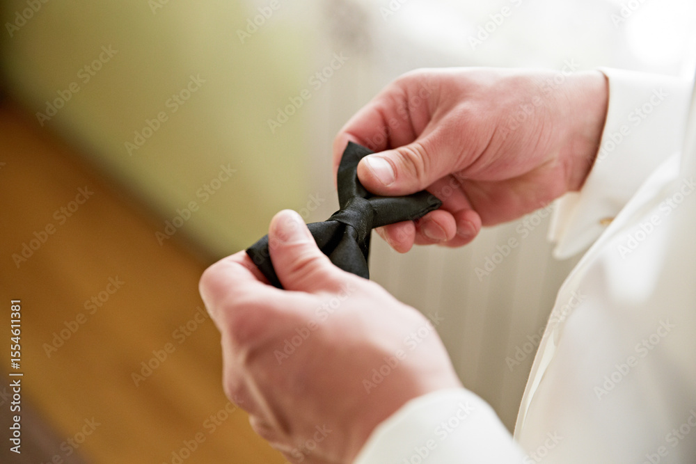 Fototapeta premium A man is getting ready for a formal event and is adjusting his black bow tie. Concept of elegance and sophistication, as the man carefully prepares himself for the occasion