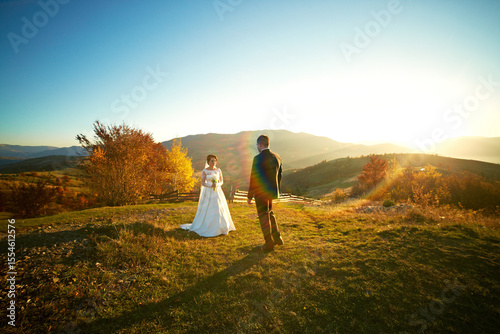 Wallpaper Mural A bride and groom stand on a grassy hillside, with the sun shining brightly behind them. The scene is serene and picturesque, with the couple looking out over the landscape Torontodigital.ca