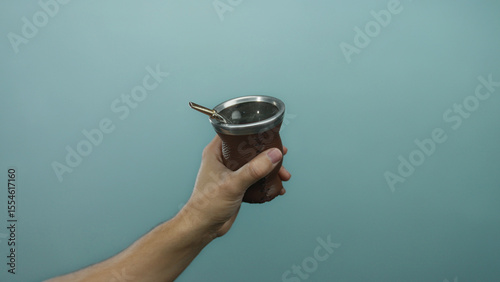 Man holding a traditional brown mate cup against a blue background, emphasizing cultural beverage in hand.