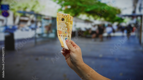Hand holding philippine pesos outdoors on a city street, symbolizing money, business, and investment opportunities in an urban setting.