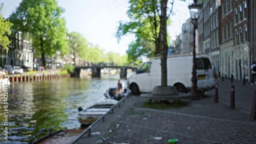 Photography Blurred view of amsterdam canal with defocused background showing a white van and a boat on a sunny day
