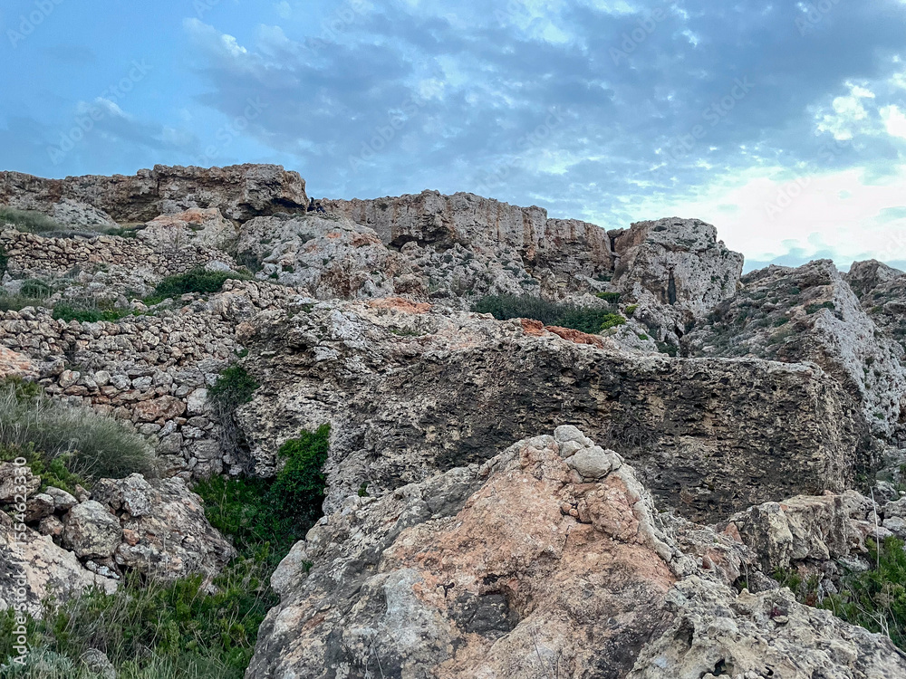 Fototapeta premium Rocky limestone terrain with sparse vegetation under a partly cloudy sky
