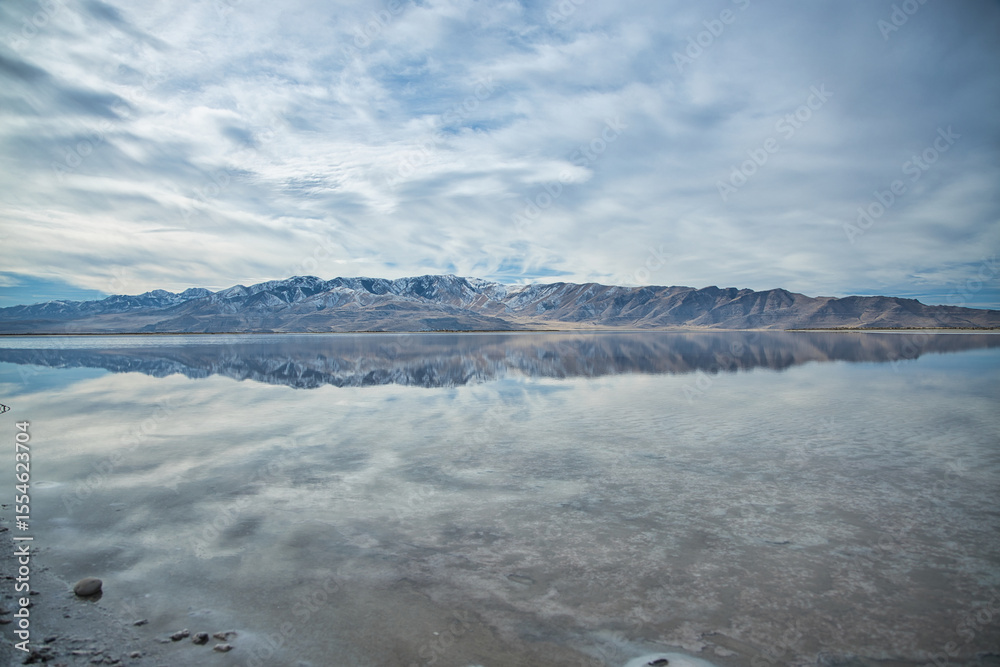 Fototapeta premium Vibrant autumn-sky hues paint the shoreline of Utah’s Great Salt Lake. Calm blue waters mirror cotton‑cloud skies, while distant mountains stand quietly, embracing seasonal wonder.
