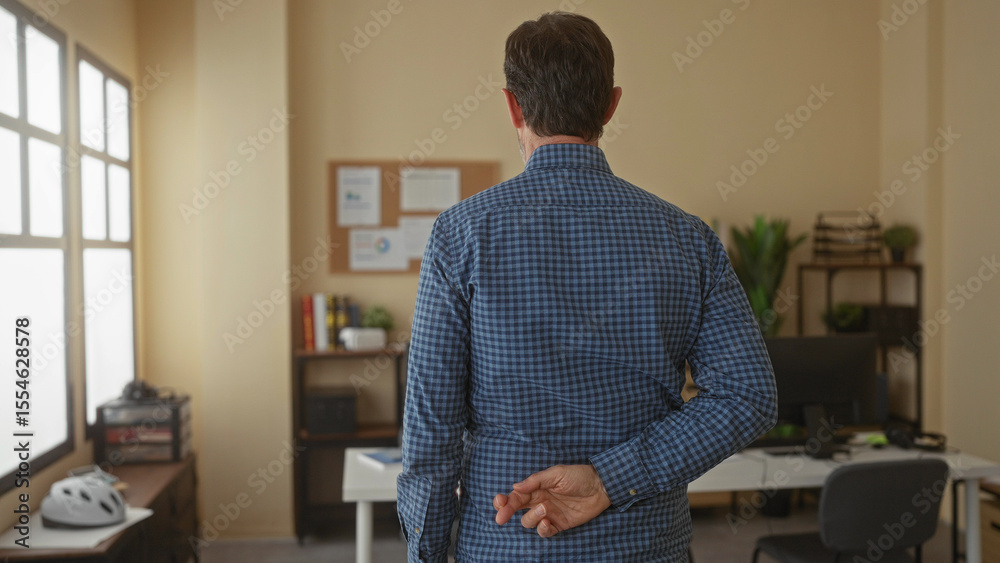 Fototapeta premium Man standing in office with crossed fingers behind back, implying deception or secrecy, surrounded by desk, chair, books, plants, and bright windows enhancing the setting.