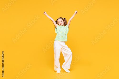 Full body little kid child girl 8-9 years old wear green t-shirt do winner gesture celebrate clench fists raise up hands isolated on plain yellow background Mother's Day love family lifestyle concept
