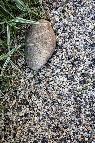 Textured Pebble Surface with Large Stone and Grass Blades. The image emphasizes natural elements and balance, ideal for backgrounds, gardening visuals, or spa and relaxation themes.