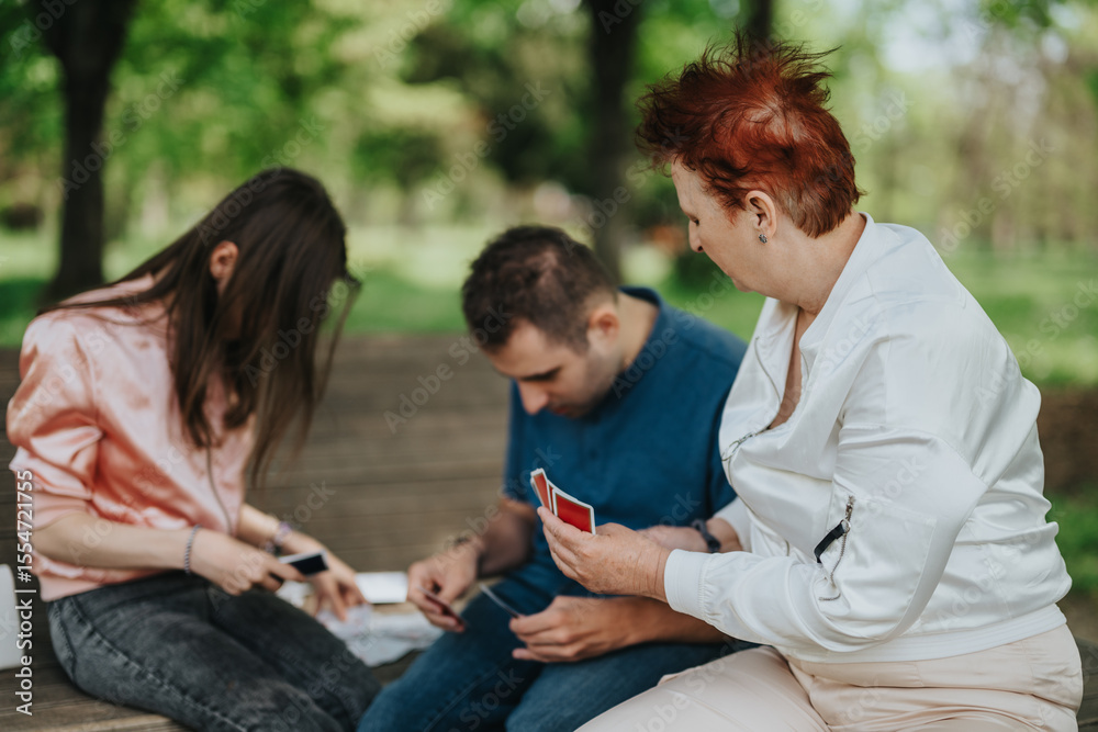 Obraz premium A close-knit family spending quality time outdoors playing a card game together, surrounded by nature, illustrating happiness, connections, and the beauty of shared moments.