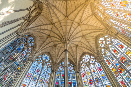 The intricate ceiling and vibrant stained glass windows of the Chapter House showcase the stunning architectural details of Westminster Abbey in London during daylight.