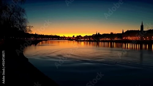 Evening cityscape reflecting in calm water, with sunset colors illuminating the horizon.