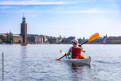 Woman kayaking on Riddarfjärden in Stockholm, with the iconic City Hall (Stadshuset) rising above the waterfront in the background.