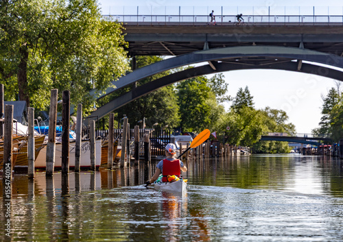 Photography Woman kayaking through Pålsundet between Långholmen and Södermalm in Stockholm, passing beneath the arches of Västerbron