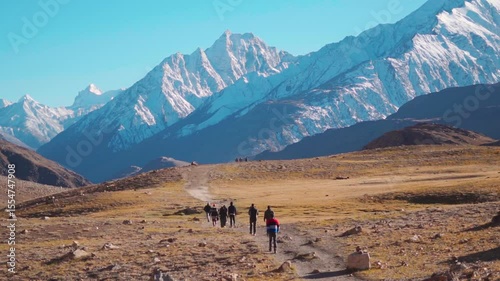 Rear view shot of group of people walking towards the snowy Himalayan mountain peak near Chandratal Lake in Spiti Valley, Himachal Pradesh, India. Group of hikers walking in front of the Himalayas.