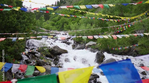 Slow motion shot of a water stream in the Himalayan mountains with prayer flags waving above it as seen near Triloknath village in Pattan valley, Himachal Pradesh, India. Scenic view of waterfall. 