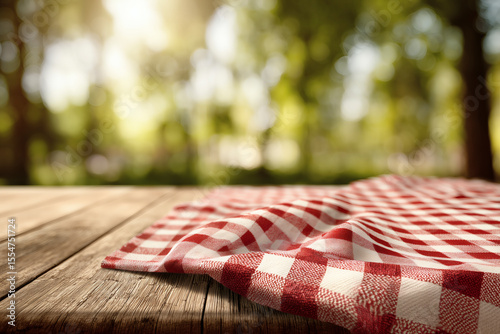 Rustic wooden table with a red and white checkered tablecloth in a sunlit outdoor setting, picnic scene.