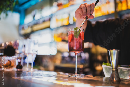 Wallpaper Mural Bartender preparing a refreshing strawberry cocktail with ice and mint in a tall glass at a stylish bar. Blurred bottles in background. Close-up on hands and drink. Torontodigital.ca