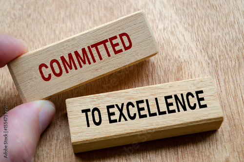 Fingers align wooden blocks that declare commitment to EXCELLENCE, reinforcing an unshakable focus on quality and continuous progress