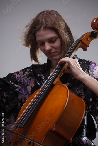 Woman playing cello, wearing floral robe, close-up portrait.
