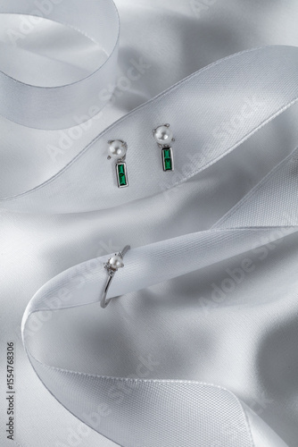 Stunning arrangement of emerald and silver earrings along with a matching ring rests on soft, lustrous fabric, showcasing a luxurious style perfect for a special occasion.