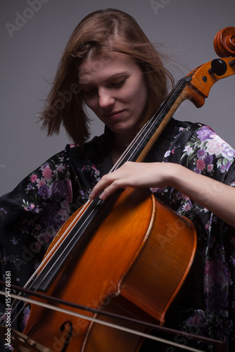 Woman playing cello, wearing floral kimono, studio shot.