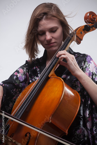 Woman playing cello, wearing floral robe, studio shot.