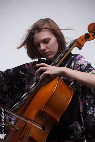 Woman playing cello, wearing floral kimono, against white background.