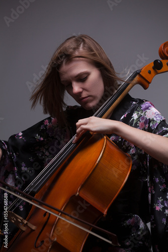 Woman playing cello, wearing floral kimono, studio shot.