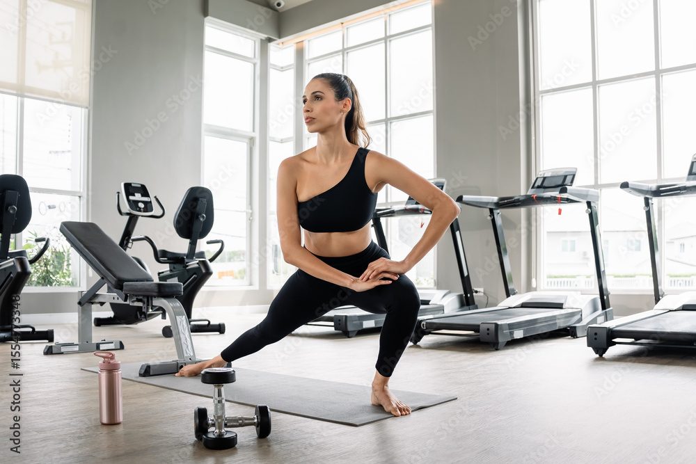 Fototapeta premium A woman is doing a yoga pose in a gym. She is wearing a black tank top and black pants