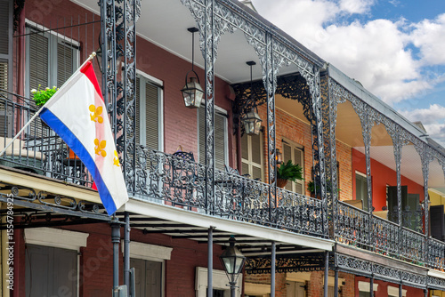Slika na platnu NOLA flag with gold Fleur-de-Lis and architecture with balconies and columns ado
