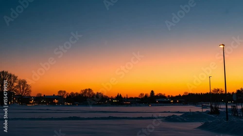 Serene winter sunset over a snowy landscape with glowing streetlights and distant buildings