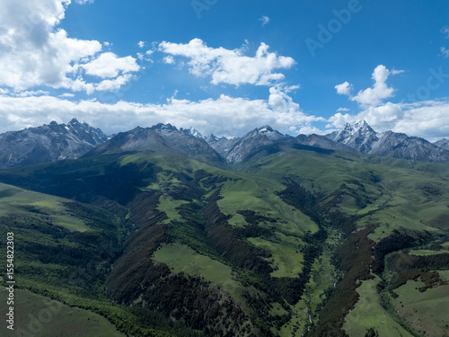 Aerial view of beautiful high altitude snow capped mountains and forest grassland landscape in China