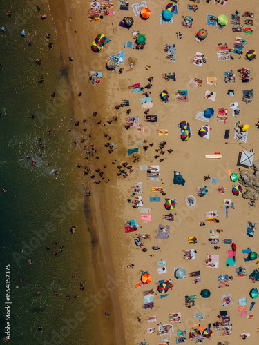Aerial drone top down view of a crowded beach with colorful umbrellas and sunbathers during a summer afternoon near the coast