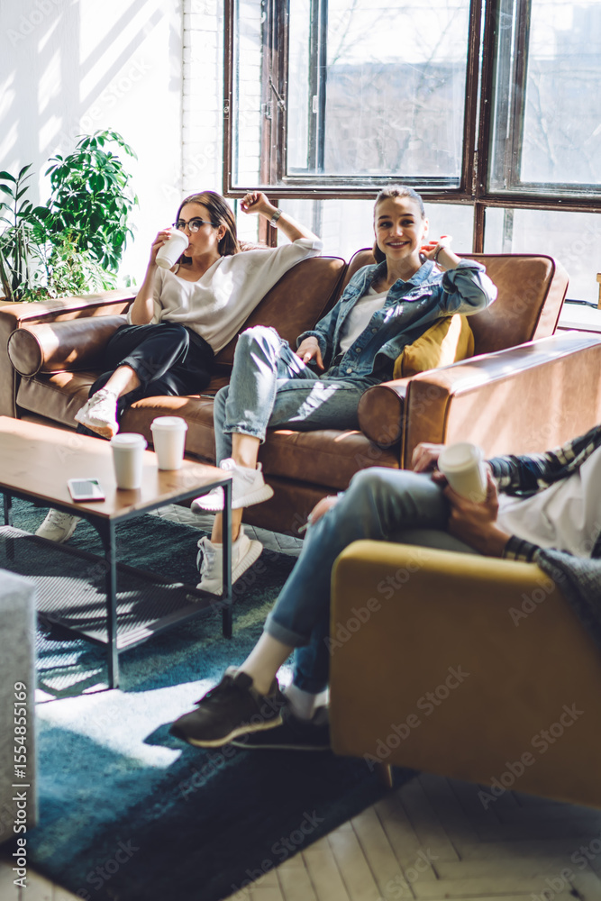 © BullRun - Cheerful friends resting on couch and using laptop at home