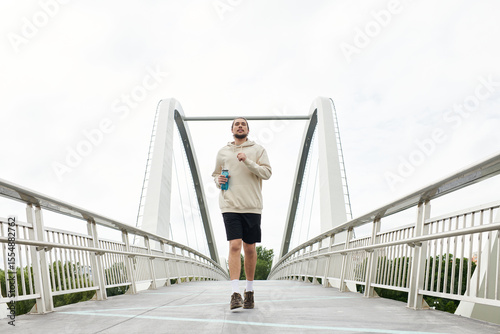 Fotografija Sporty young man jogging on a bridge while enjoying the outdoors in a hoodie