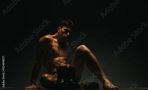 Canvastavla Artistic depiction of a fit, muscular man sitting on the floor in subdued ambient lighting, emphasizing the contours of his figure and the focused atmosphere