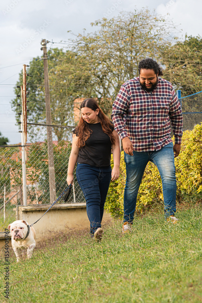 Obraz premium Bulldog leading his owners on a joyful park walk. walking and enjoying the sunshine. Surrounded by grass and greenery, they share laughter and play