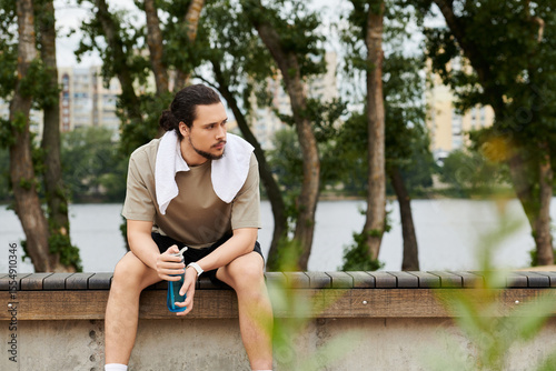 Sporty young man with beard takes a break during outdoor workout by the water