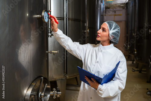 Female wine enologist inspecting modern stainless steel barrel fermentation for quality control in wine factory production