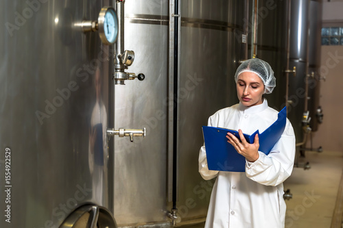 Female wine enologist inspecting modern stainless steel barrel fermentation for quality control in wine factory production