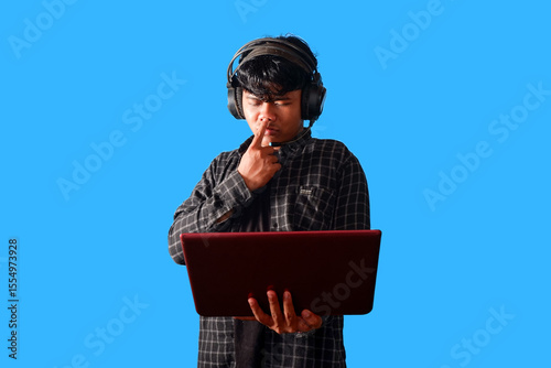 Focused Young Man Using Laptop and Headphones, Concentrated Expression  isolated on blue background
