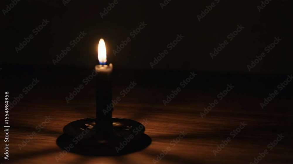 Black candle on a wooden table with flickering shadows in dark setting, camera zoom and out-of-focus