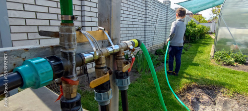 Child watering backyard garden with hose on sunny day. sustainable lifestyle and outdoor activity concept