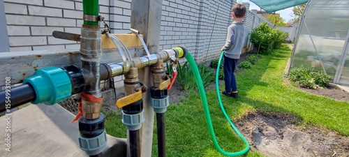 Child watering backyard garden with hose on sunny day. sustainable lifestyle and outdoor activity concept