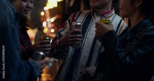 A group of young people are drinking beer on a city street. They laugh and clink cans together.