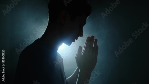 Silhouette of desperate man praying in dim blue light, expressing emotional breakdown and spiritual seeking in solitude.