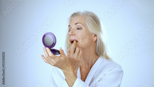 A mature woman is smiling and applying makeup with a brush, radiating happiness in a bright and soothing spa environment. She appears relaxed and content.
